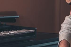 Άνδρας μουσικός συνθέτει μελωδίες παίζοντας κιθάρα σε studio με πλήκτρα και υπολογιστή
